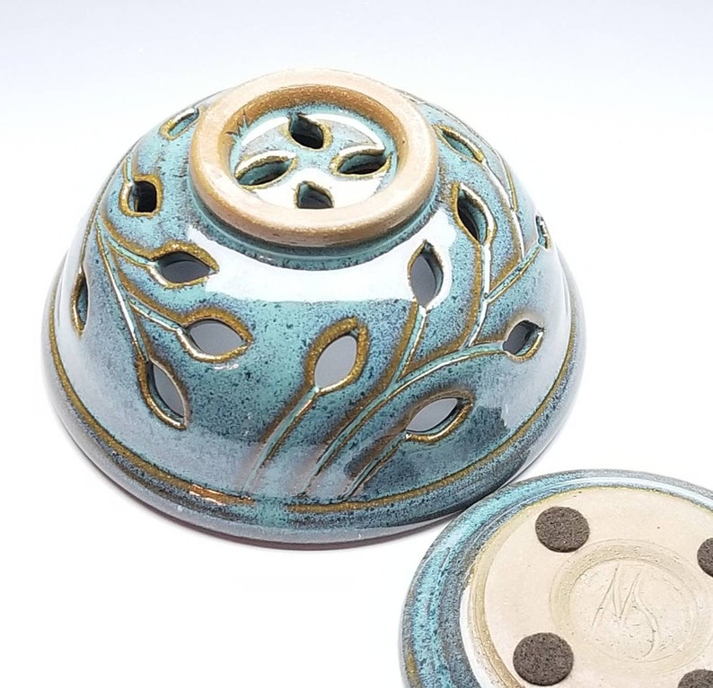 May include: A teal blue ceramic incense burner with a leaf design and a small hole in the top. The burner has a matching base with four small feet.