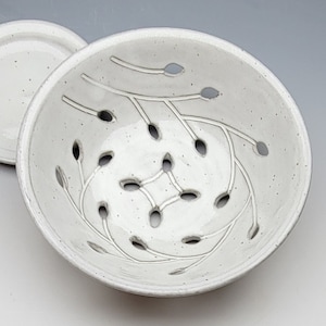 May include: White ceramic colander with a leaf design and holes for draining. The colander is round and has a white glaze.
