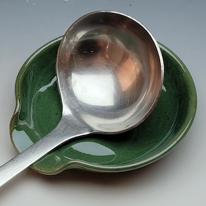 May include: A green ceramic spoon rest with a silver ladle resting in it.