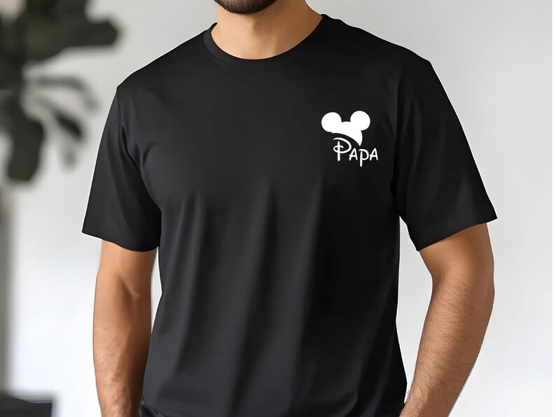 May include: Black t-shirt with a white graphic of Mickey Mouse ears and the word "PAPA" in a stylized font. The shirt is short-sleeved and made of a soft material.