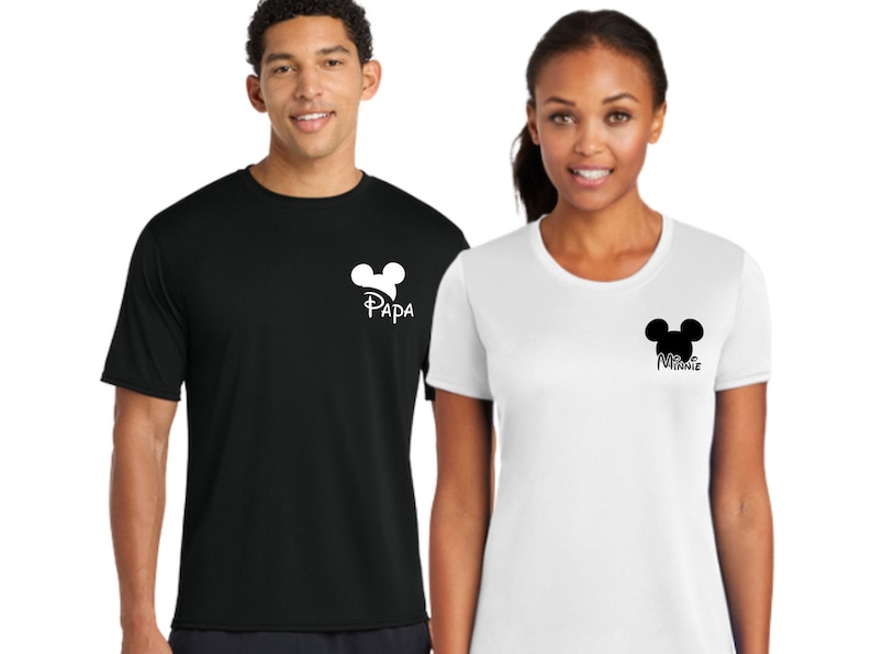 May include: Black and white t-shirts with a Mickey Mouse head design. The black shirt has the word "Papa" and the white shirt has the word "Minnie". Both shirts are short-sleeved and worn by two people.