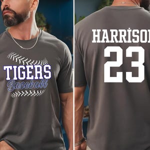 May include: Gray baseball t-shirt with "TIGERS Baseball" text on the front and "HARRISON 23" on the back. The front design includes a baseball graphic. The shirt is short-sleeved.