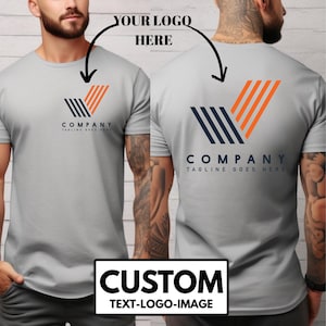 May include: Light gray t-shirt with a company logo on the front and back. The logo is a stylized V shape with navy blue and orange stripes. The text "COMPANY TAGLINE GOES HERE" is below the logo. The bottom of the shirt has the text "CUSTOM TEXT-LOGO-IMAGE".