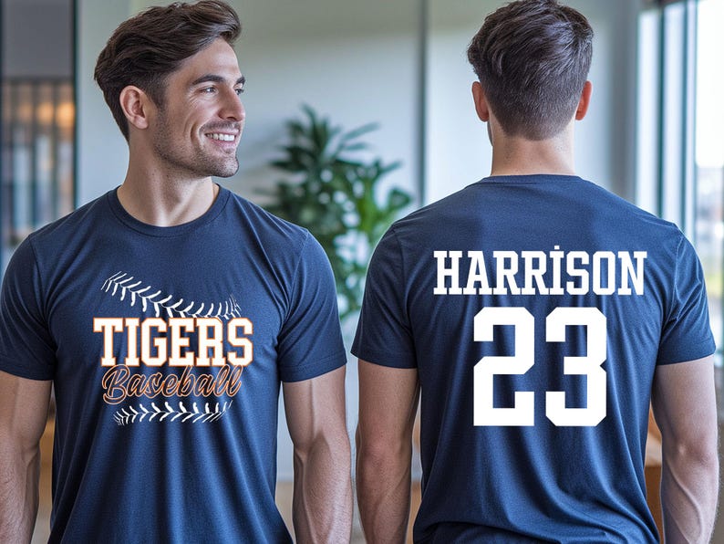 May include: Navy blue baseball t-shirt with "TIGERS Baseball" in orange and white lettering on the front. The back of the shirt displays "HARRISON 23" in white. The shirt is worn by a person.