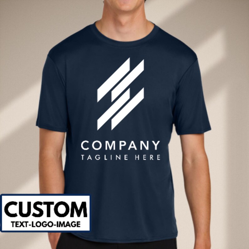 May include: Navy blue short-sleeve t-shirt with a white geometric logo and the text "COMPANY TAGLINE HERE". The shirt also has a white rectangle with the word "CUSTOM" and the text "TEXT-LOGO-IMAGE".