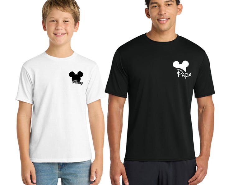 May include: Two short-sleeved t-shirts, one white and one black. The white shirt has a black Mickey Mouse head silhouette with the word "Mickey" below it. The black shirt has a Mickey Mouse head silhouette with the word "Papa" below it.