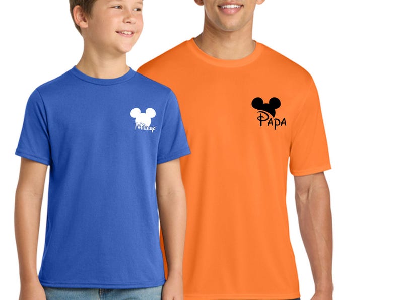 May include: Two short-sleeved t-shirts, one blue and one orange. The blue shirt has a white Mickey Mouse head design with the word "Mickey" below it. The orange shirt has a black Mickey Mouse head design with the word "Papa" below it.