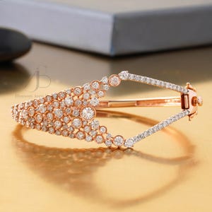 Könnte beinhalten: Armband aus Roségold mit Diamantbesatz. Das Armband hat eine Reihe von runden Diamanten, die zusammengefasst sind, mit einem geometrischen offenen Design. Der Verschluss ist ebenfalls mit Diamanten verziert.