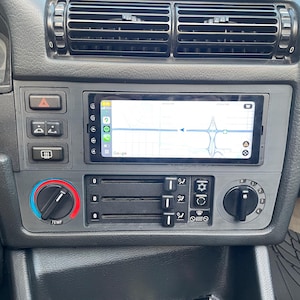 Puede incluir: Panel de instrumentos negro de coche con un moderno sistema de infoentretenimiento que muestra un mapa con navegación. El panel incluye controles de climatización, luces de emergencia y otros botones. La pantalla muestra la interfaz de Google Maps.