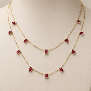 Puede incluir: Un collar de cadena de oro de doble capa con múltiples piedras preciosas de color rojo intenso, de corte rectangular y espaciadas uniformemente. Los delicados eslabones dorados conectan cada piedra roja, creando un efecto escalonado.