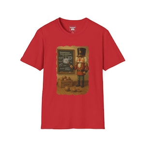 May include: Red t-shirt featuring a graphic of a nutcracker in a military uniform, standing in front of a chalkboard. The chalkboard has text and a diagram. A box of nuts is below the chalkboard.