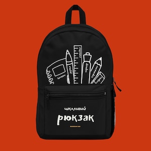 Op de afbeelding: Zwarte rugzak met een voorvak en een handvat aan de bovenkant. De rugzak heeft een witte illustratie van schoolspullen, waaronder een notitieboek, pen, liniaal, stift en potlood. De tekst "школьный рюкзак" is op de voorkant gedrukt.