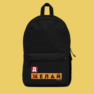 Op de afbeelding: Zwarte rugzak met een voorvak met ritssluiting en een zijvak van gaas. De rugzak heeft een patch met Russische tekst in oranje en wit. De tekst bevat het woord "ЖЕЛАЙ" en de Russische letter "Д".