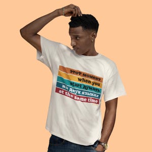 May include: White t-shirt with a colorful text design. The text reads "Этот момент when you start думать на двух языках at the same time" in a mix of Russian and English. The shirt is being worn by a person.