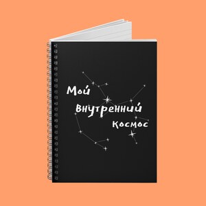 May include: A spiral-bound notebook with a black cover featuring white text and constellation designs. The text reads "Мой внутренний Космос", which translates to "My Inner Cosmos". The notebook's pages are white.
