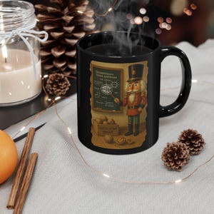 Könnte beinhalten: Schwarze Keramik-Tasse mit einer farbenfrohen Illustration eines Nussknackers in roter und goldener Uniform, der vor einer Tafel mit russischem Text steht. Die Tasse hat einen großen Henkel und ist mit einem dampfenden Getränk gefüllt.
