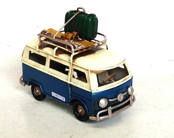 May include: A miniature blue and white van with a luggage rack, a green suitcase, and skis on top. The van has black wheels and a license plate that reads "2110D-3720". The van's body is blue and white, with a distressed, vintage look.