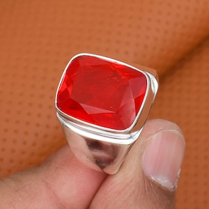 May include: A silver ring featuring a large, rectangular, faceted red gemstone. The gemstone is set in a polished silver band. The ring is a bold statement piece, suitable for adding a pop of color to any outfit.