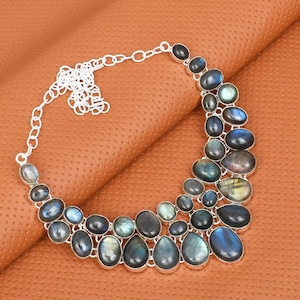 May include: A silver necklace featuring multiple oval and teardrop-shaped labradorite stones in shades of blue, gray, and green. The stones are set in a silver metal frame and connected by a silver chain.