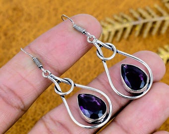 May include: A pair of sterling silver dangle earrings featuring a teardrop-shaped faceted purple amethyst gemstone set within a polished silver frame. The earrings have a hook-style closure and a looped metal design above the stone setting.