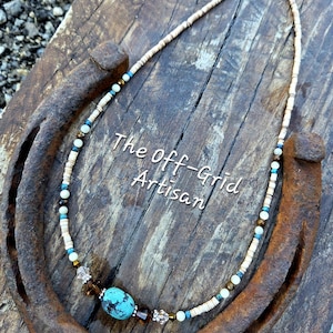 May include: A handcrafted necklace with a turquoise stone and various beads. The necklace is displayed on a rustic horseshoe and wooden surface. The text "The off-Grid Artisan" is visible.