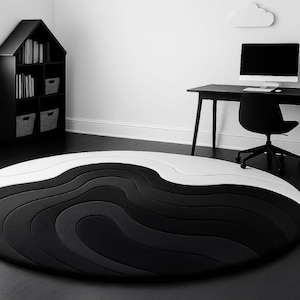 May include: A contemporary, circular rug with a distinctive layered design in black, grey, and white. The rug's wavy pattern creates a striking visual contrast. The room also features a black desk, chair, and bookshelf.