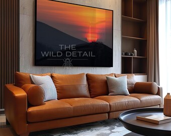 Könnte beinhalten: Ein großes, gerahmtes Kunstwerk, das einen Sonnenuntergang über einer Bergkette zeigt, hängt über einem braunen Ledersofa. Das Kunstwerk zeigt einen leuchtend orangefarbenen und roten Himmel. Das Sofa hat mehrere Kissen und einen runden Couchtisch davor. Der Text "THE WILD DETAIL" ist sichtbar.