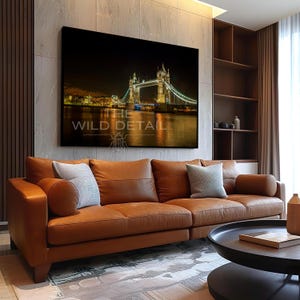 Pode incluir: Uma grande tela do Tower Bridge em Londres à noite, iluminada com luzes douradas e brancas, está pendurada acima de um sofá de couro castanho. O texto "THE WILD DETAIL" é visível. O quarto tem um design moderno.