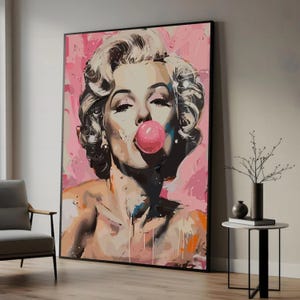 Op de afbeelding: Groot ingelijst kunstwerk van een vrouw die een kauwgomballenblaas blaast. Het kunstwerk heeft een roze en wit kleurenpalet met verfsplatters. De vrouw heeft blond haar en draagt weinig kleding.