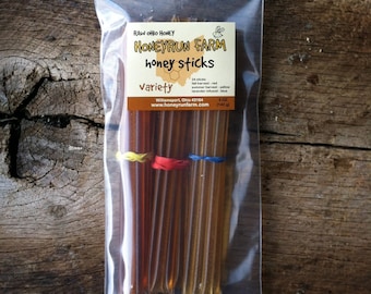 Pode incluir: Um saco de plástico transparente contendo 24 palitos de mel. Os palitos estão dispostos em um feixe e amarrados com três elásticos amarelos, vermelhos e azuis. O saco tem um rótulo que diz "RAW OHIO HONEY HONEYRUN FARM honey sticks Variety 24 sticks fall harvest - red summer harvest - yellow lavender infused - blue Williamsport, Ohio 43164 www.honeyrunfarm.com 5 OZ (142 g)"