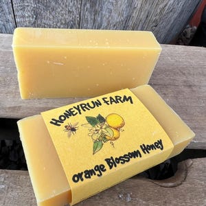 May include: Two bars of honey, one wrapped in yellow paper with the text "Honeyrun Farm Orange Blossom Honey" and a bee and orange blossom illustration.