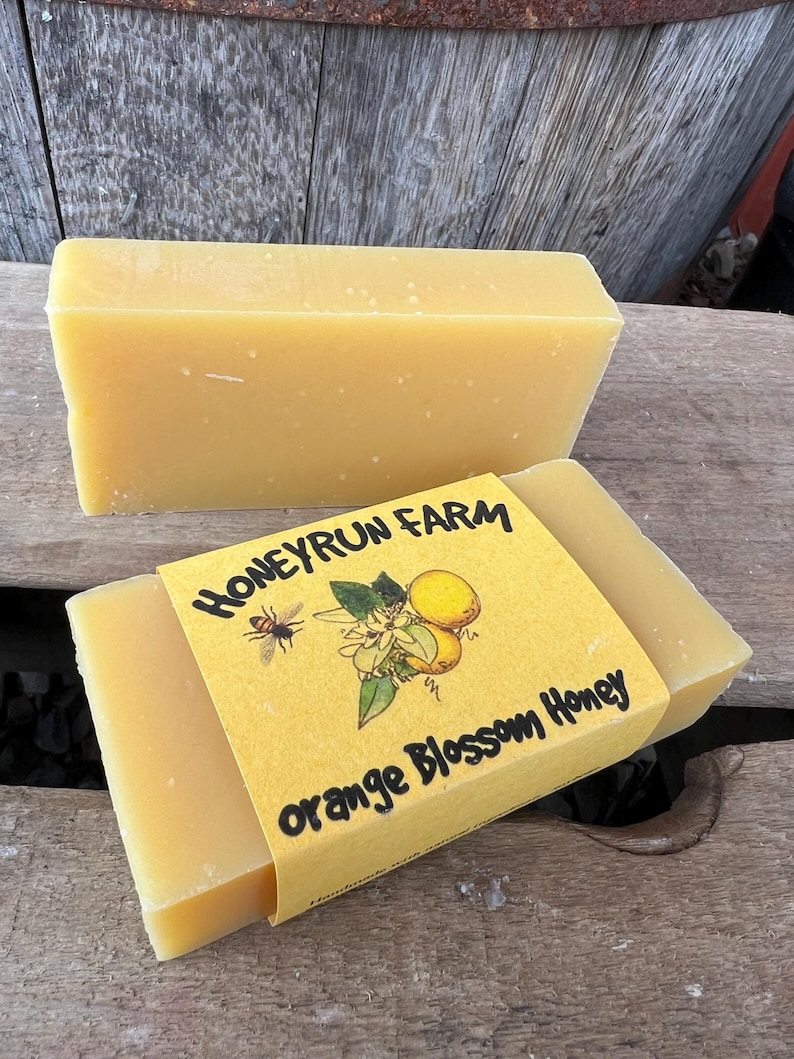 May include: Two bars of honey, one wrapped in yellow paper with the text "Honeyrun Farm Orange Blossom Honey" and a bee and orange blossom illustration.