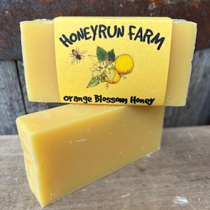 May include: A yellow bar of soap with a label that reads "Honeyrun Farm" and "Orange Blossom Honey". The label features a bee and orange blossoms.