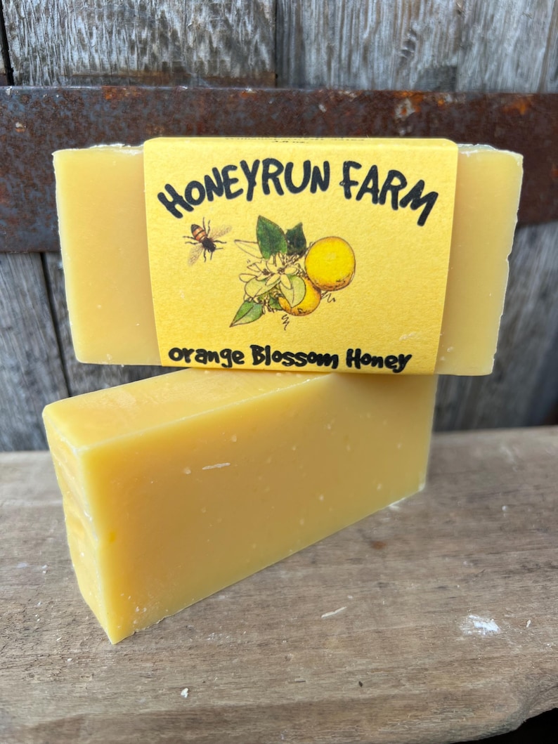 May include: A yellow bar of soap with a label that reads "Honeyrun Farm" and "Orange Blossom Honey". The label features a bee and orange blossoms.