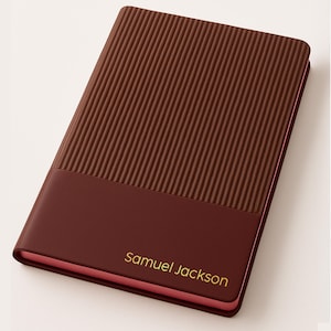 May include: A brown leather-bound journal with a textured, ribbed cover. The lower portion of the journal is a solid brown color, with the name "Samuel Jackson" in gold lettering. The edges of the journal are pink.