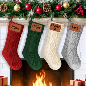 May include: Four cable-knit Christmas stockings in red, green, cream, and gray, each with a personalized leather patch. The stockings hang above a fireplace decorated with garland and ornaments. The names on the patches are Mom, Emily, Charlie, and Dad.
