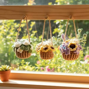 Könnte beinhalten: Drei gehäkelte Hängekörbe mit Blumenarrangements. Die Körbe sind braun, und die Blumen sind weiß, gelb und lila. Jeder Korb hängt an einem Holzdübel mit einer naturfarbenen Kordel. Eine kleine Sukkulente im Topf steht auf der Fensterbank.