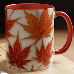 May include: An 11 oz ceramic mug with a white background and a repeating pattern of orange and red maple leaves with gold outlines. The interior and handle are red.