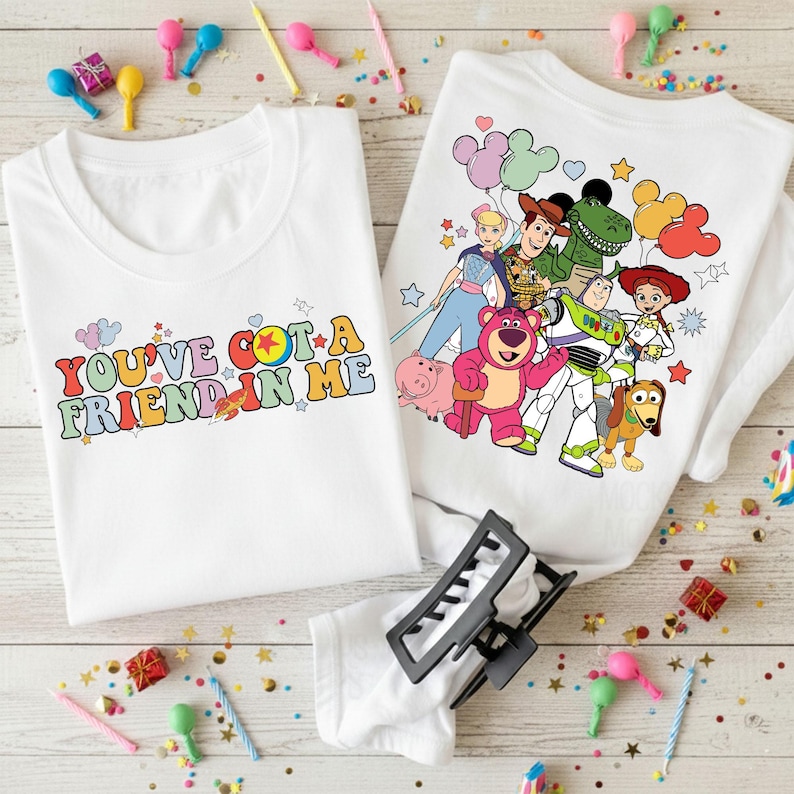 May include: Two white t-shirts with colorful graphics. One shirt has the text "YOU'VE GOT A FRIEND IN ME" in retro font. The other shirt features characters from the Toy Story movie. Party decorations are scattered around the shirts.