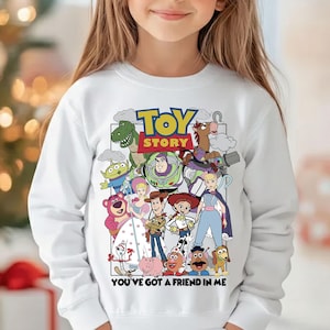 May include: White sweatshirt with a vibrant graphic of characters from the animated film "Toy Story." The design includes the film's title and the phrase "You've Got a Friend in Me." The sweatshirt is a long-sleeved crew neck.