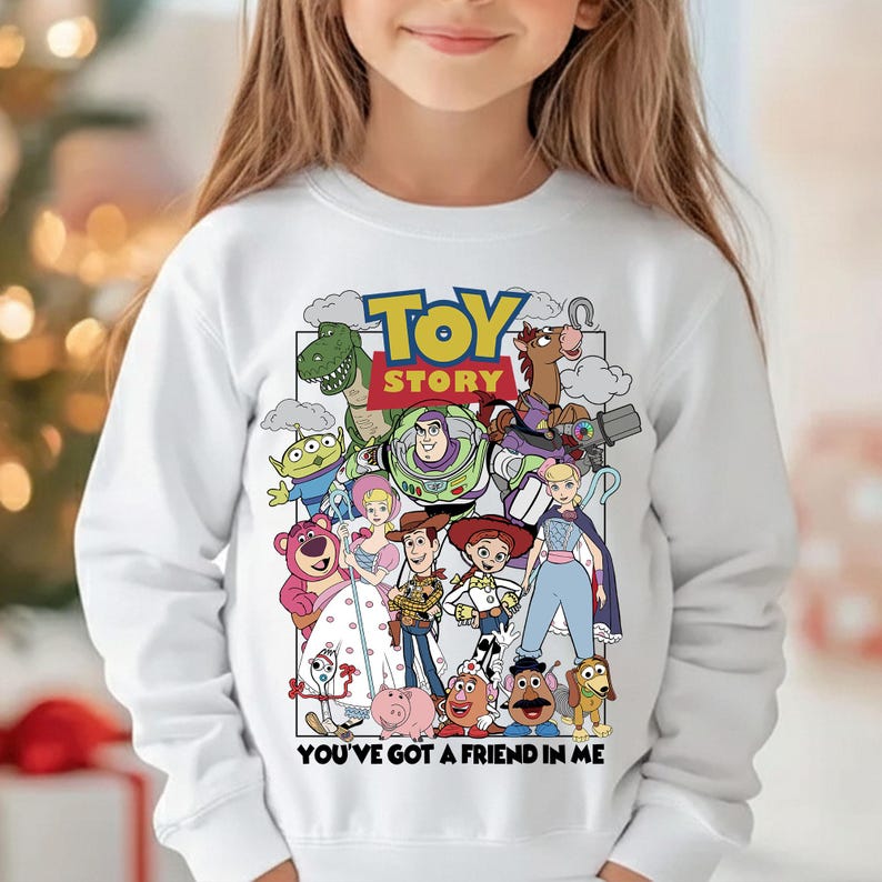 May include: White sweatshirt with a vibrant graphic of characters from the animated film "Toy Story." The design includes the film's title and the phrase "You've Got a Friend in Me." The sweatshirt is a long-sleeved crew neck.
