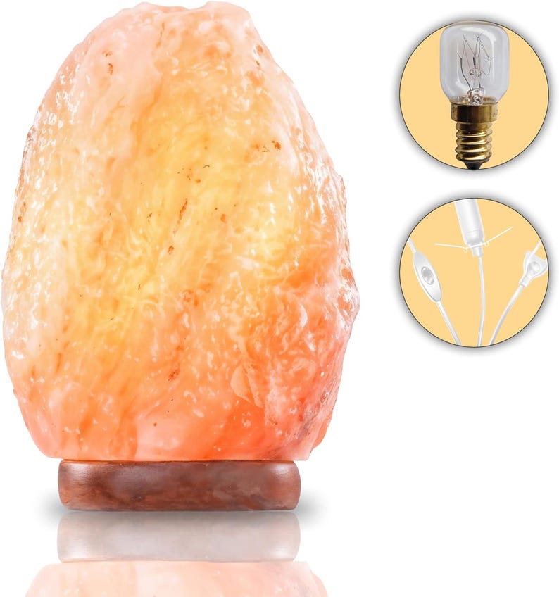 Peut inclure: Une lampe de sel de l'Himalaya avec une surface rugueuse, orange-rose, mont&eacute;e sur une base en bois fonc&eacute;. La lampe est allum&eacute;e, d&eacute;gageant une lueur chaleureuse. Comprend une ampoule et un cordon d'alimentation.