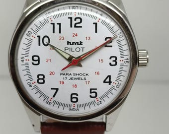 May include: A silver-toned wristwatch with a white face, black numerals, and red second hand. The watch features the text "hmt PILOT" and "PARA SHOCK 17 JEWELS". It has a brown leather strap.