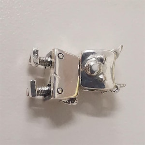 May include: A silver-colored metal clasp with a rectangular design. The clasp features two screws and a square-shaped component with a rounded top. The metal has a shiny finish, and the clasp appears to be a jewelry component.
