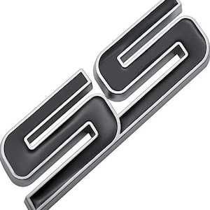 Op de afbeelding: Zwart en zilver SS-embleem. Het embleem heeft een zwart interieur met een zilveren omtrek. De letters zijn gestileerd en lijken van metaal te zijn. Het embleem is waarschijnlijk voor een voertuig.