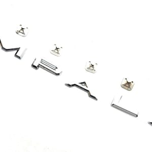 Può includere: Lettere metalliche cromate e hardware di montaggio su sfondo bianco. Le lettere compongono la parola "ALFA" e sono accompagnate da diverse piccole clip di montaggio quadrate. Le lettere hanno una finitura metallica riflettente.