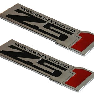 May include: Two rectangular metal emblems with the text "PERFORMANCE PACKAGE" and "NS1" in black. The emblems have a silver finish with a red accent on the right side. The background is white.