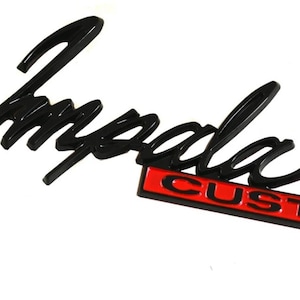 May include: Black Impala emblem with the word "Impala" in a cursive font. Below it is a red rectangle with the word "CUSTOM" in white letters. The emblem is likely for a car.