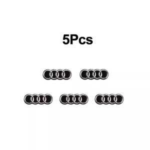 Puede incluir: Cinco emblemas de coche negros y plateados sobre un fondo blanco. Los emblemas son el logotipo de Audi, que consta de cuatro anillos entrelazados. El texto "5Pcs" está encima de los emblemas.