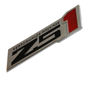 Puede incluir: Un emblema plateado y negro Z51 Performance Package con un acento rojo. El emblema es rectangular con el texto "PERFORMANCE PACKAGE" encima de las letras grandes "Z51".